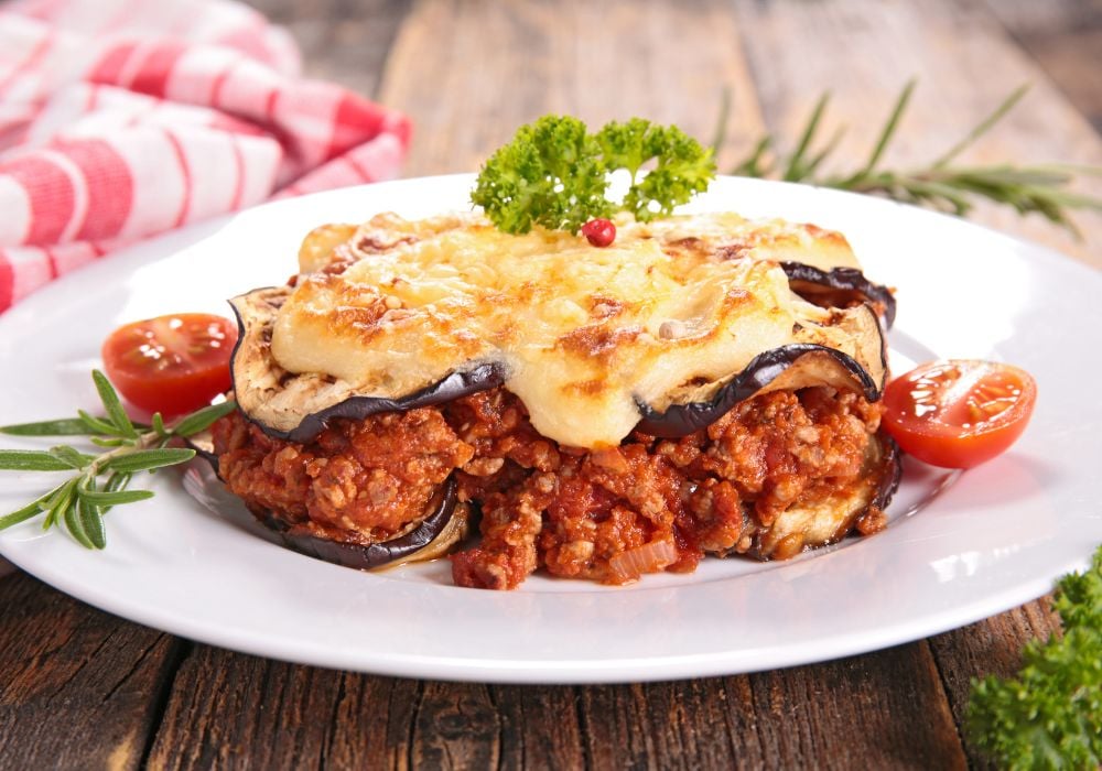 Greek Moussaka served in white ceramic plate with some parsley aside