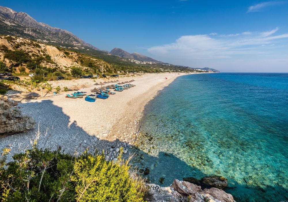 A beautiful white sandy beach in Dhermi with sunbeds and umbrellas.