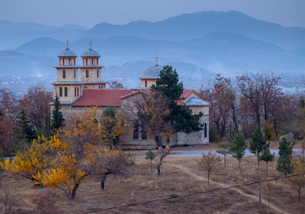 A church on top of a hill in Korce, Albania, with a view of the mountains that surround the city in the background. 