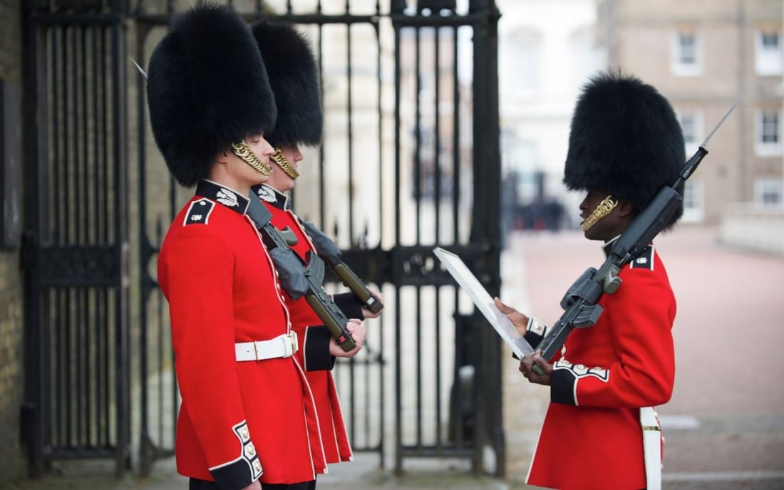 Royal guards in red jackets confer at the entrance to Clarence House on Pall Mall.